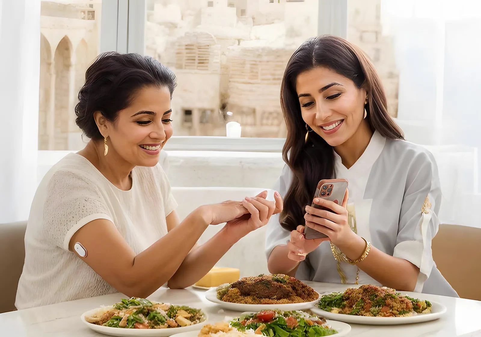 Two women at a meal, one wearing the GS1 sensor on the back of her upper arm, checking the SIBIONICS app